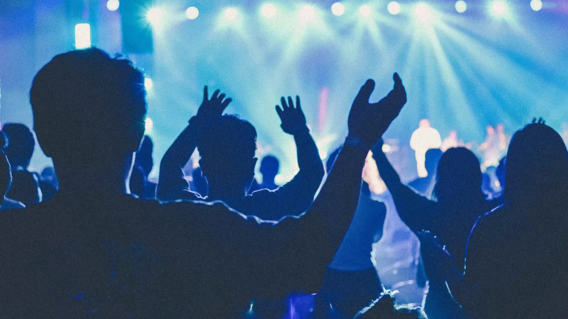 A worship crowd with hands raised under stage lights