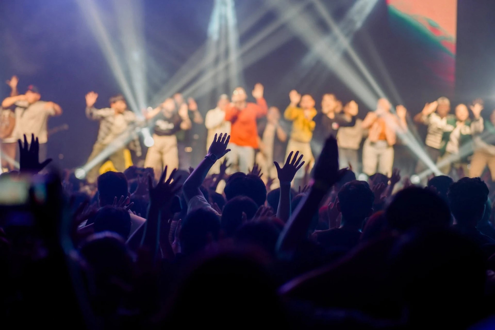 A worship crowd with hands raised toward performers on a brightly lit stage